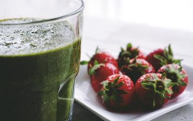 Strawberries displayed on a white plate beside a green smoothie in a tall glass