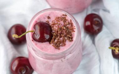 Pink cherry smoothie in a glass mason jar topped with a whole cherry and show chocolate shavings.