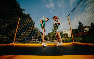 Two kids jumping on an outdoor trampoline in summer.
