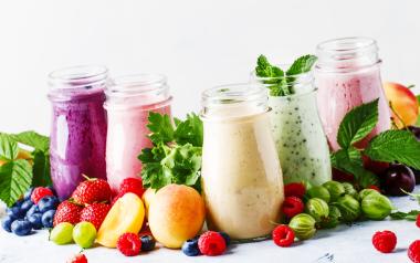 A variety of smoothies displayed on a surface covered in berries and other fruits.