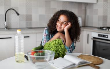 A teen sits at a kitchen island with various ingredients in front of her.
