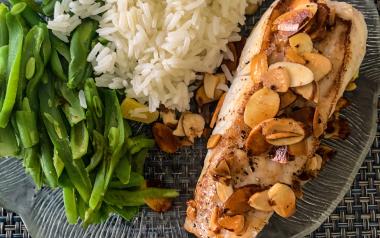 A plate with green beans, white rice, and slivered almonds atop a piece of halibut.