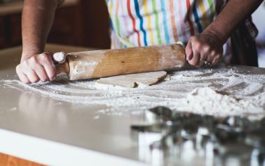 a person wearing an apron uses a rolling pin to flatten dough on a kitchen counter