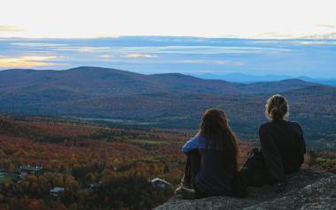 two teens sit and admire a view of trees below