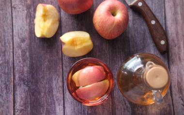 apples on a wooden table alongside a knife and jar of cider