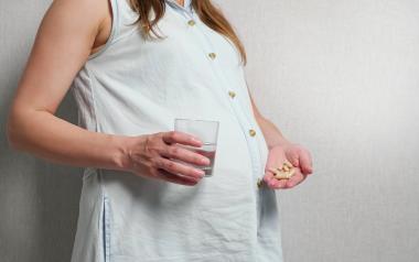 pregnant woman holding a glass of water in one hand and supplements in the other