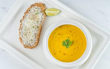 a bowl of squash soup next to a piece of bread and a lime