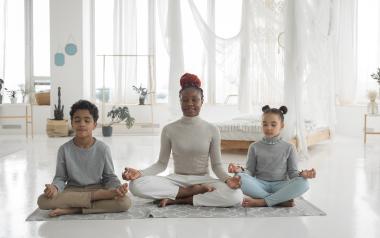 a mom and two kids meditating crosslegged on a yoga mat