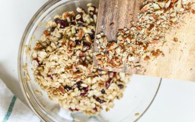 a cutting board with nuts being dumped into a mixing bowl with granola 