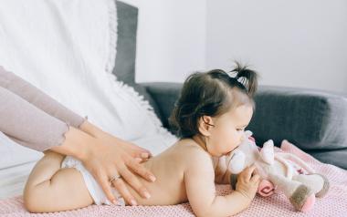 parent massaging back of infant with infant laying on stomach chewing toy