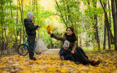 a mom offers fall leaves to child while sitting outside
