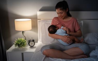 A woman sits in bed breastfeeding at night