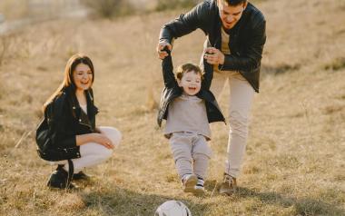 a father holds his toddler to help them kick a soccer ball