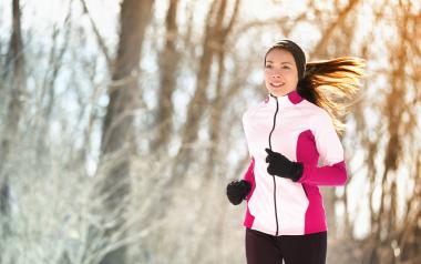 A woman running in the winter with trees in the background