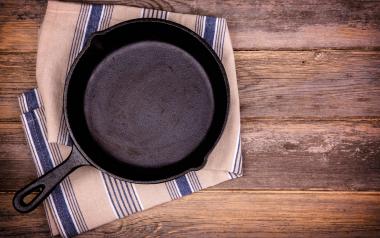 Empty cast iron skillet with tea towel, over old wood background