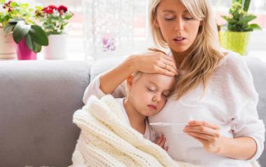 Are Fevers in Children Beneficial? mom cuddling with sick daughter and checking temperature