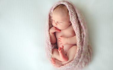 sleeping newborn baby wrapped in a pink knitted blanket