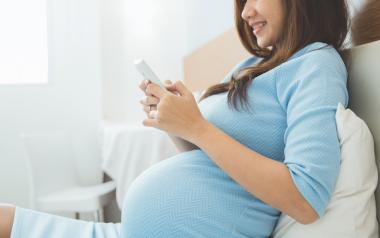 Pregnancy Apps: Smiling pregnant woman in bed using smartphone