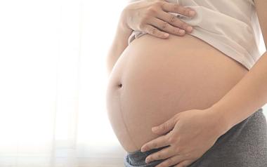 woman holding her bare, very pregnant abdomen