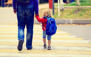 Transitioning to kindergarten: Parent holding hands with small child wearing backpack viewed from behind