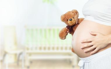 How Your Body Changes After Pregnancy: pregnant belly with woman's hand on it and teddy bear peeking out from behind