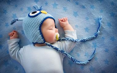 infant sleeping on back with soother and wearing a blue knitted hat