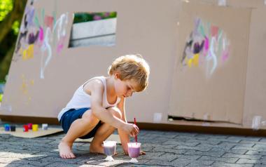 school-aged boy painting cardboard in the driveway