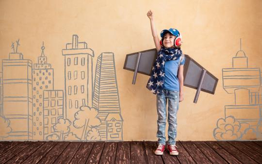 child dressed up with airplane wings against a wall with buildings drawn on it