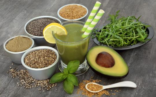 small bowls of seeds, avocado, bowl of arugula on wooden table