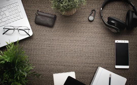 Sustainable Computing: Top view of workspace. Laptop mobile phone, wallet, headphones, women hat, notebook, pencil