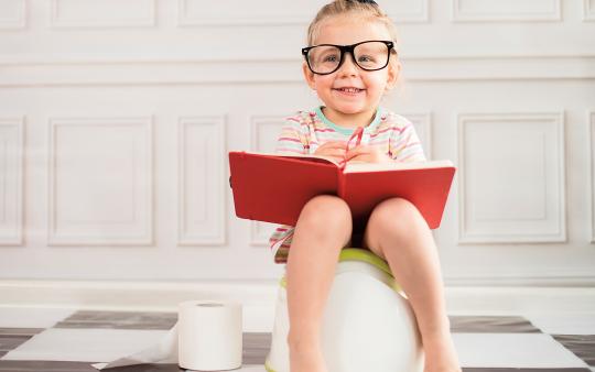 small child sitting on the potty and smiling with a red book on lap