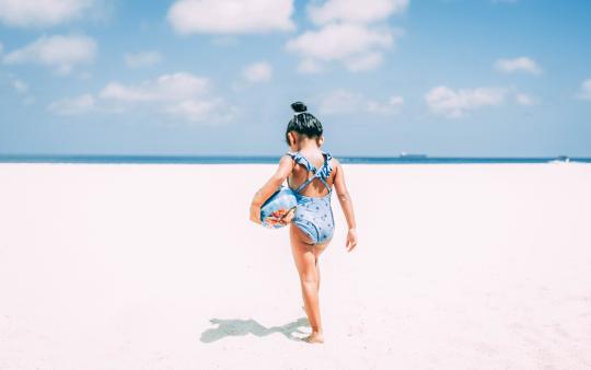 small girl holding a ball at the beach