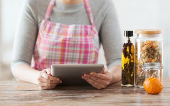 woman in apron at kitchen counter reading recipe