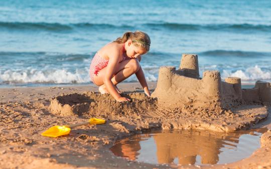 young girl building a sand castle on the beach with water behind her