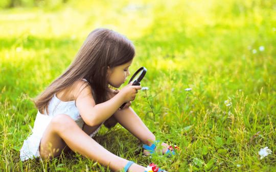 small girl sitting in the grass with a magnifying glass