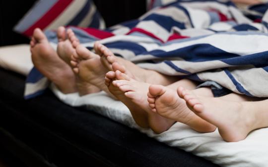 view of adults' and children's feet sticking out from beneath the bed covers