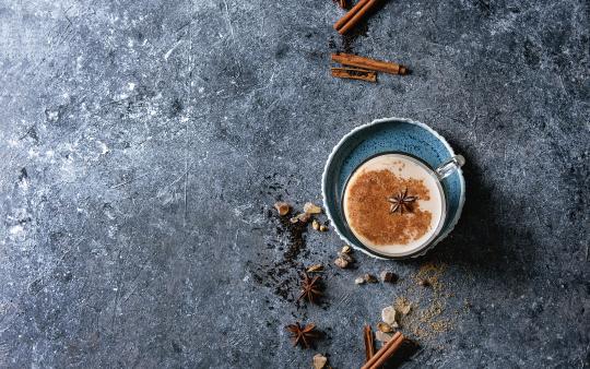 Cinnamon, cardamom, anise, sugar, black tea over dark texture background