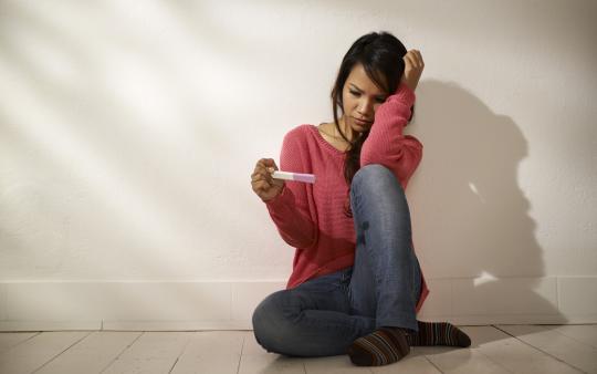 woman looking anxiously at a pregnancy test stick