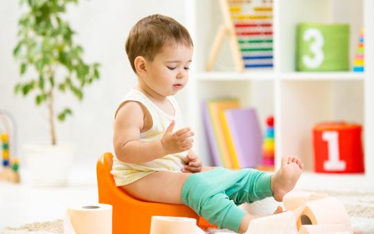 smiling baby sitting on potty with toilet paper rolls