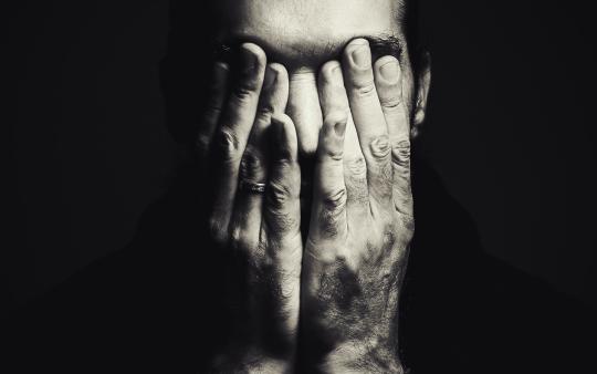 Portrait of a man with hands on face, depressed expression, in black and white.