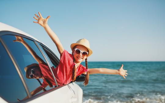 happy child poking out of car window with arms spread