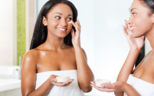 A woman wearing a towel and applying a white skincare cream to her face