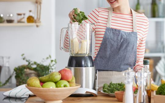 A woman in the kitchen blending ingredients to make a smoothie