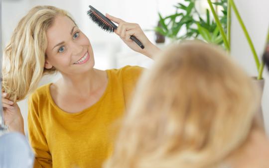 Woman brushing her long blonde hair while wearing a yellow top