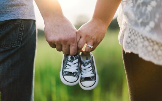 A man and woman holding a pair of baby shoes