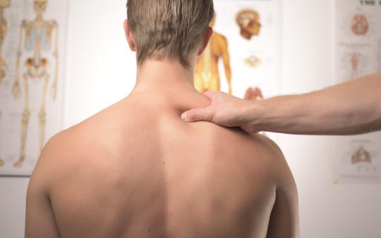 A chiropractor places a hand on the shoulder of a man