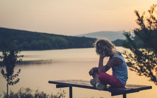 Child on a dock in summer, facing away from the camera with their head in their hand