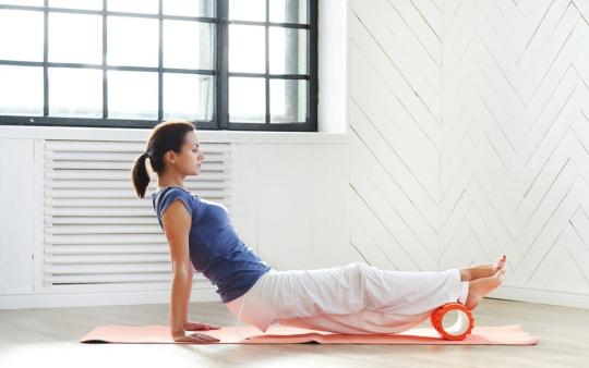 A woman using a foam roller on her lower legs.