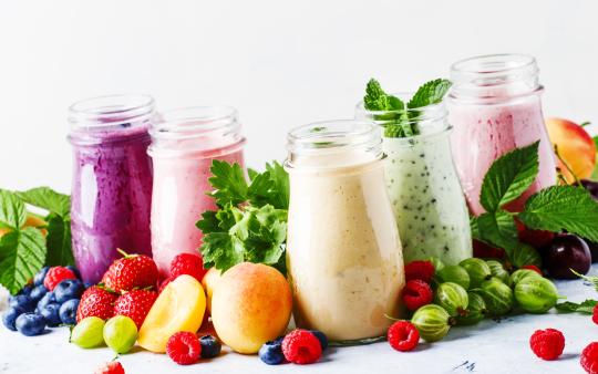 A variety of smoothies displayed on a surface covered in berries and other fruits.