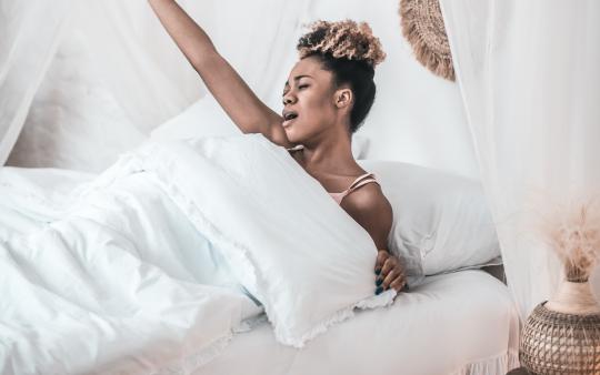 A woman stretching in a bed of white sheets.